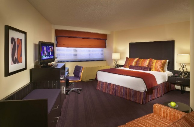 A wide-angle view of a hotel room with a bed, TV, sofa, desk, and nightstand.