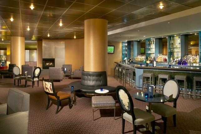 A wide view of a hotel lobby with a fireplace, bar, and seating area.